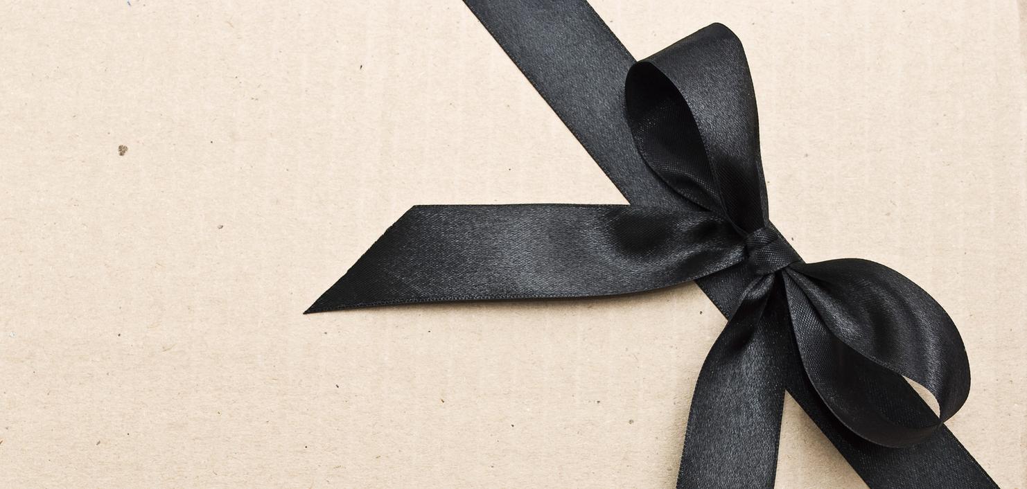 Geschenk mit schwarzem Satinband auf braunem Kraftpapier. Das Band ist zu einer Schleife gebunden.